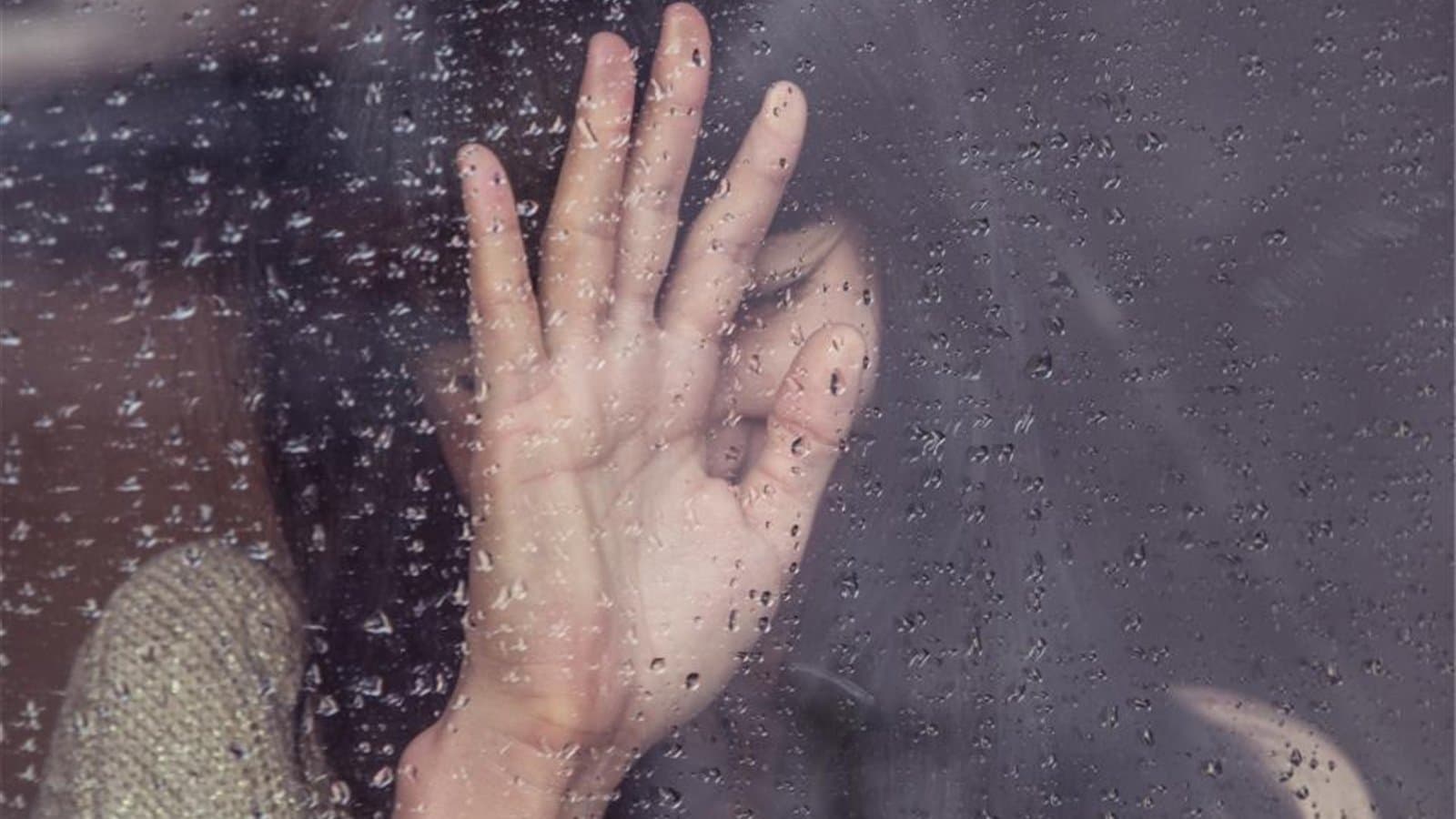 雨の窓に手を当てる人