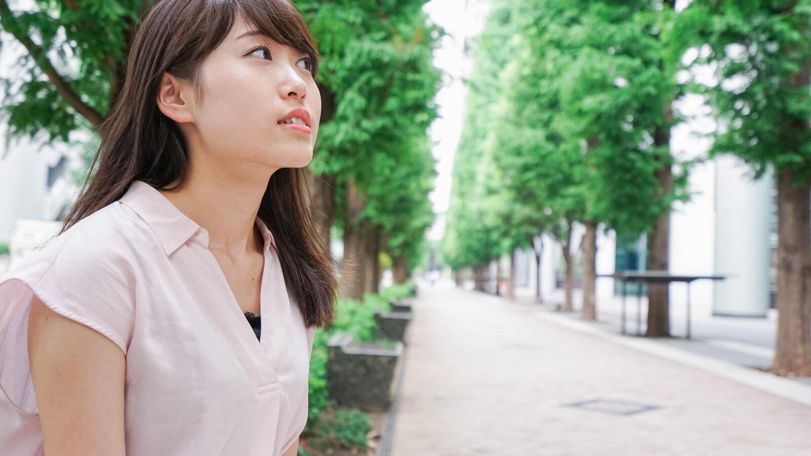 緑の並木道で一人で考え込む女性