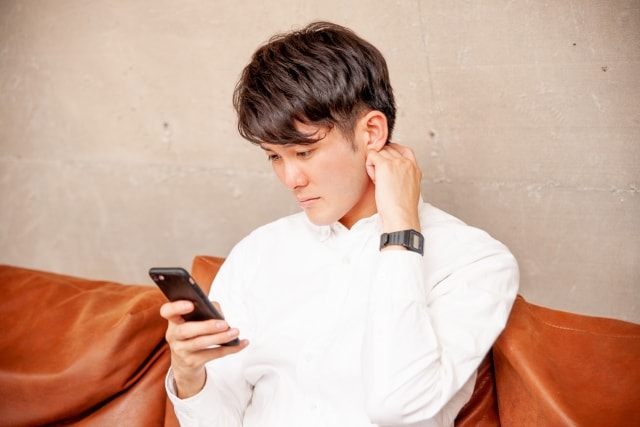 ソファでスマートフォンを見る男性