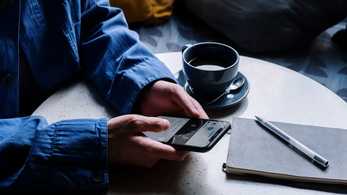 ノートを置いたカフェのテーブルでスマートフォンを操作する手元