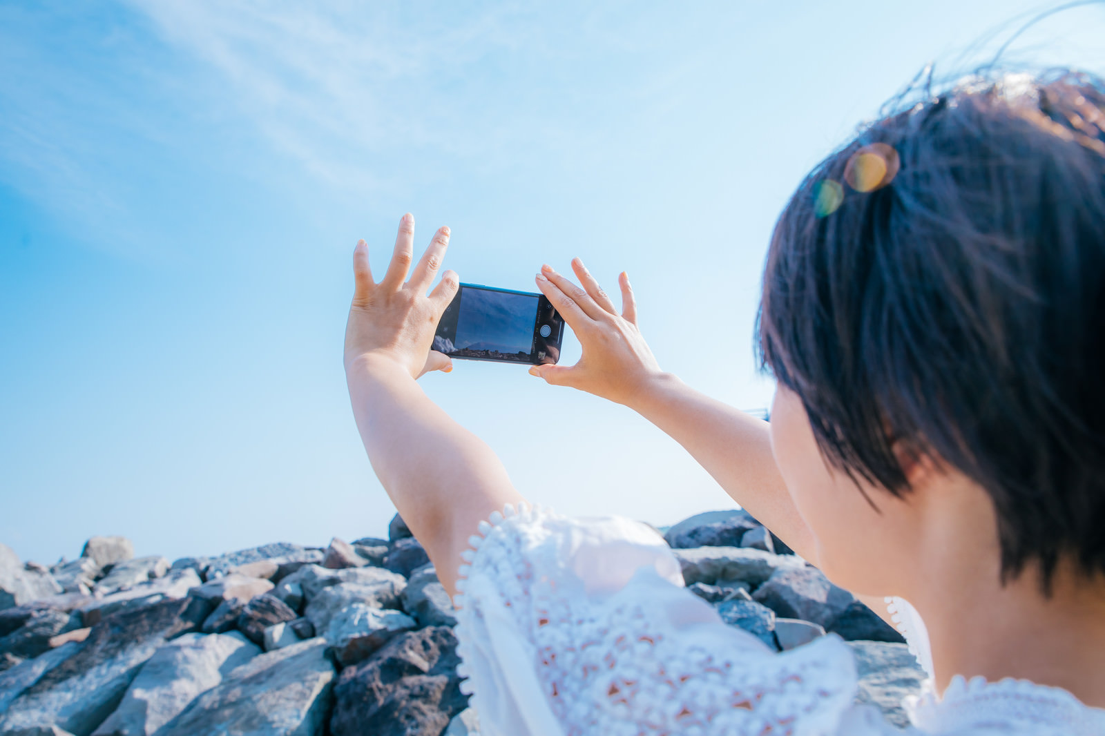 青空に向かってスマートフォンを掲げる女性