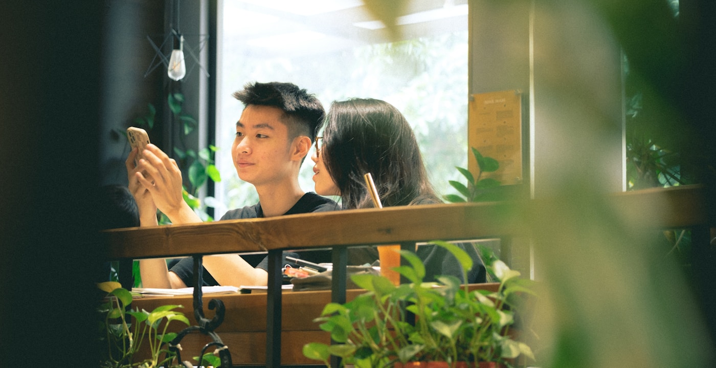 カフェでスマートフォンを見ながら話す若い二人