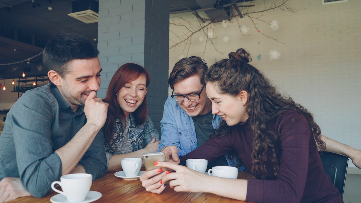 カフェでスマートフォンを見ながら会話する友人たち